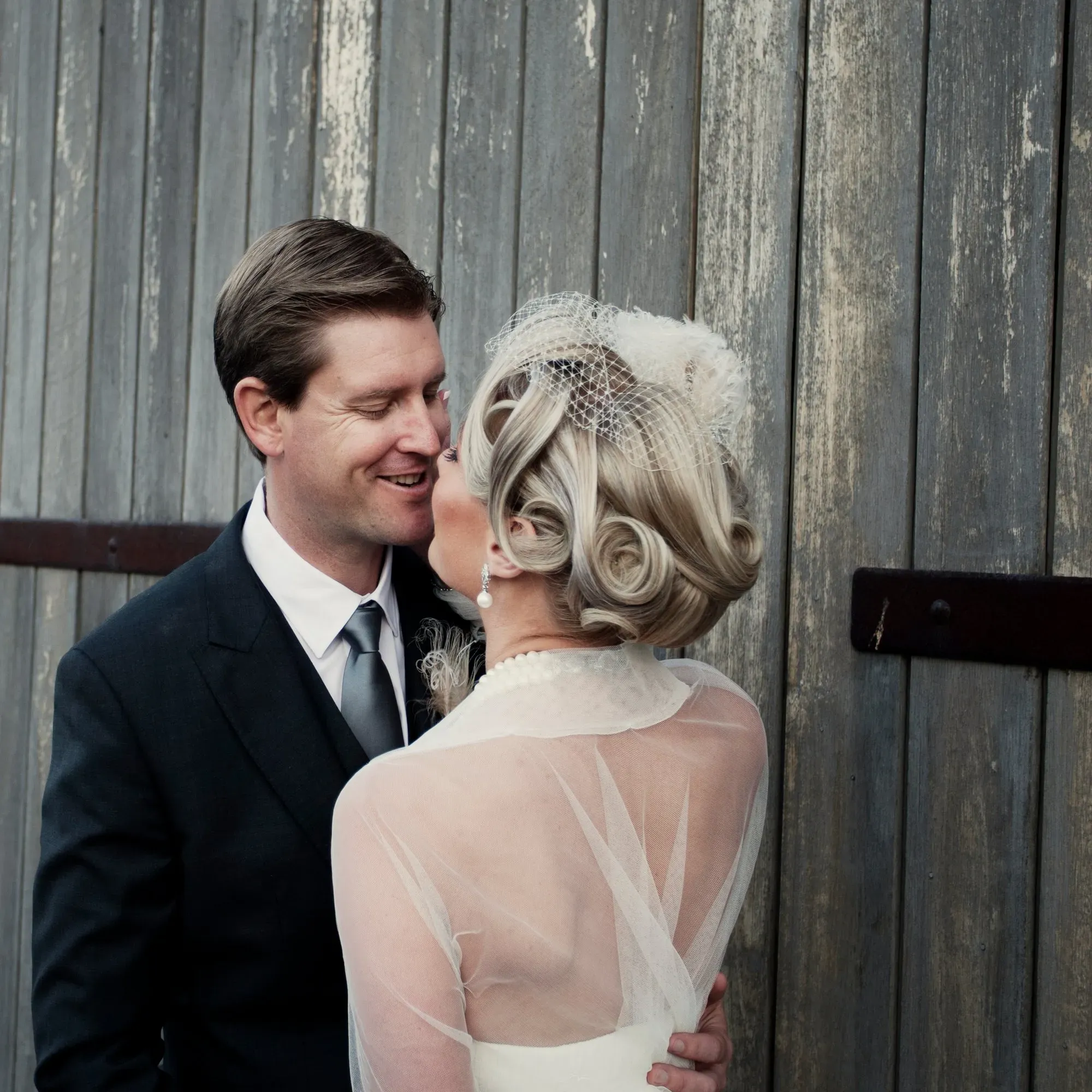 A vintage roll set under a birdcage veil, the bride with her groom against weathered timber