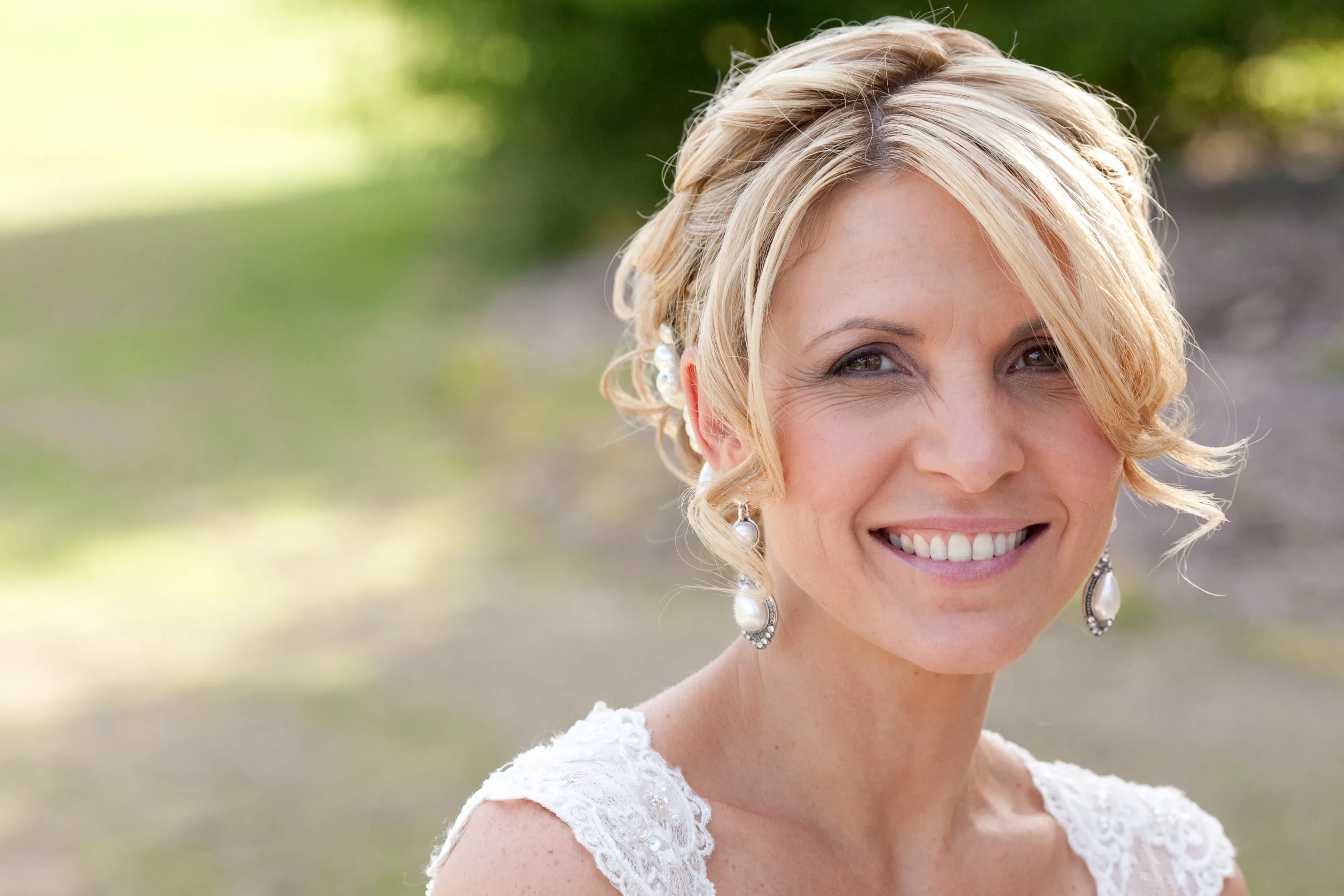 Bride with a soft textured updo and pearl earrings, hair by Bellus