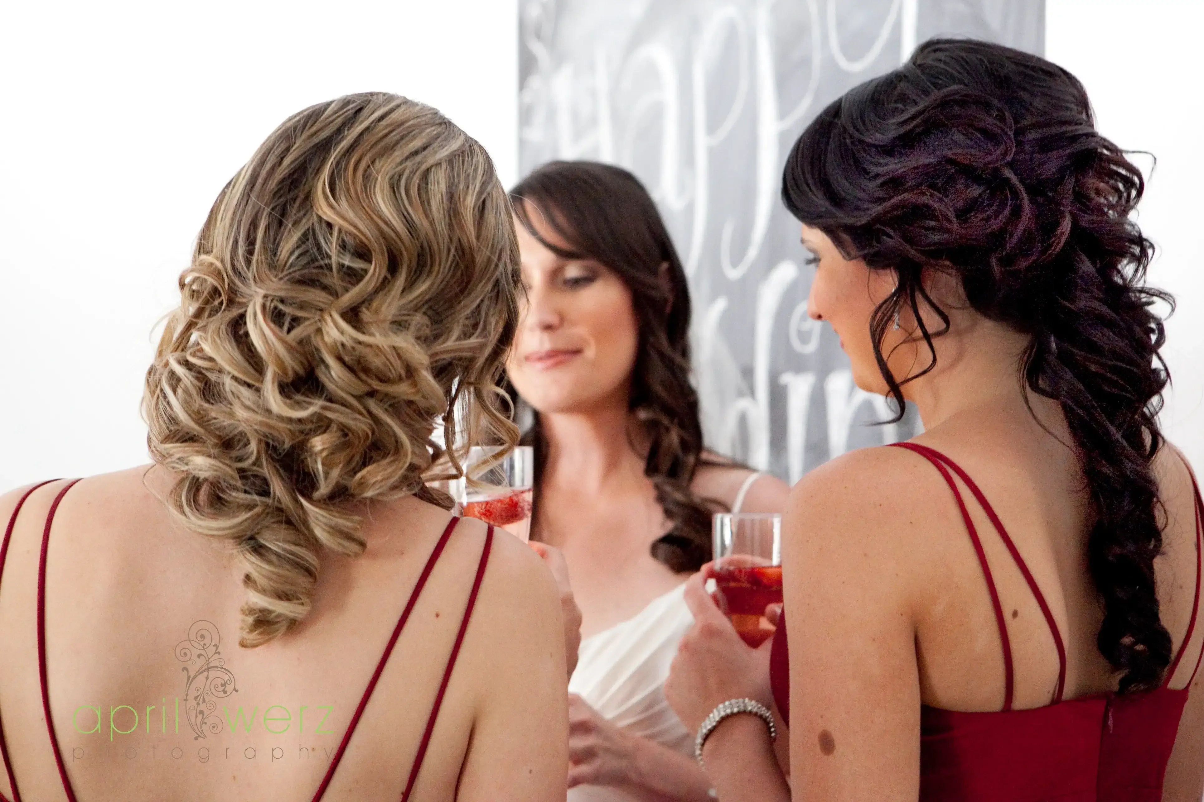 Three women photographed from behind at the reception, long bridal waves and curled lengths by Bellus